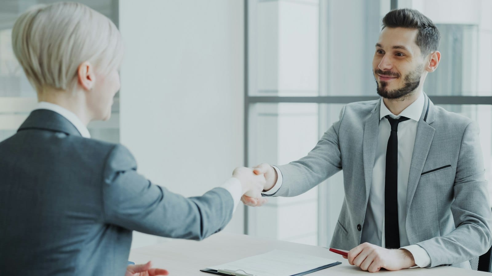 Two professionals shaking hands across a table in an office, representing a client conversation reaching agreement