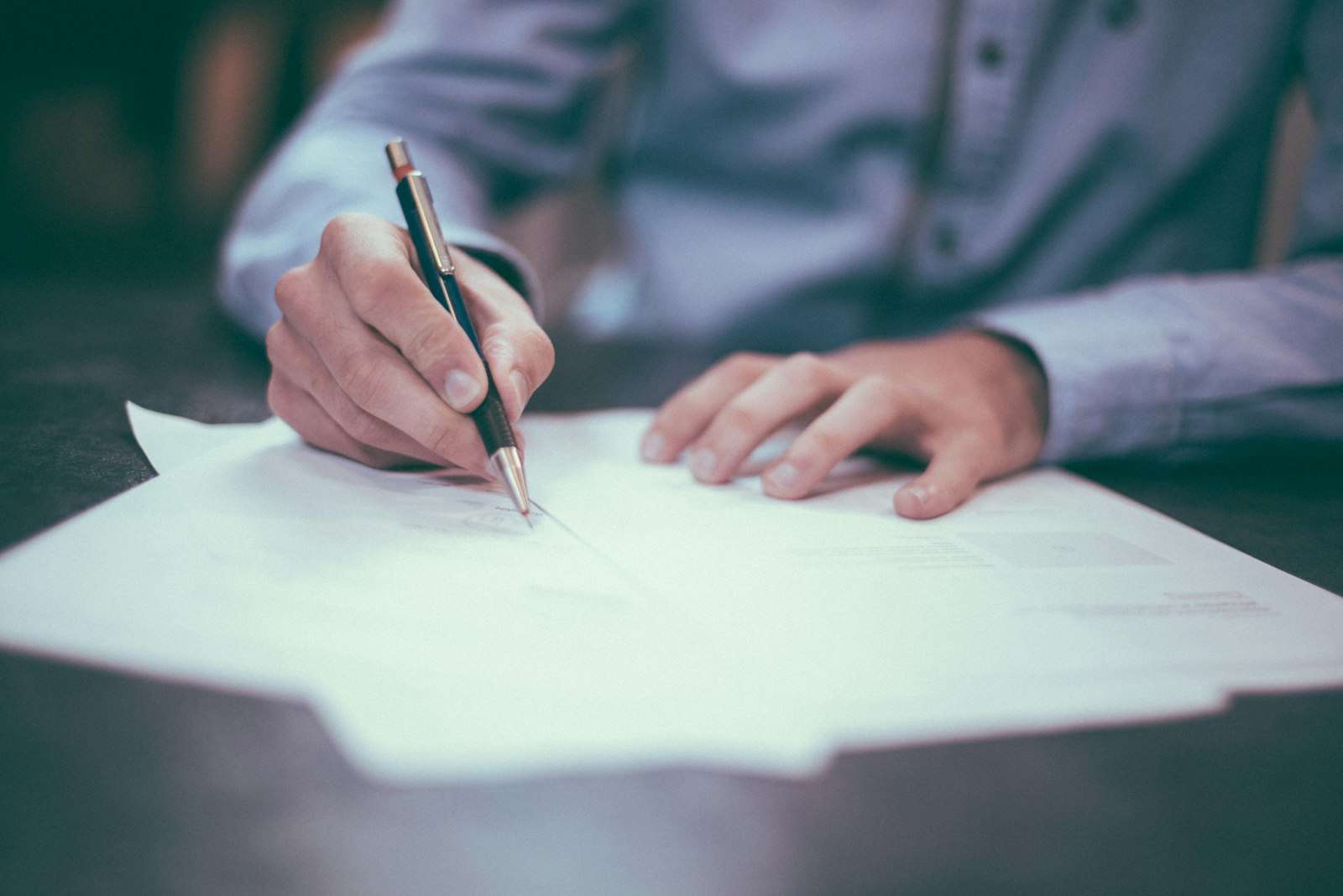 Person signing a document with a pen, representing a guarantor loan agreement